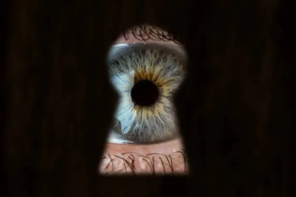 Photo of Female blue eye looking through the keyhole. Concept of voyeurism, curiosity, Stalker, surveillance and security