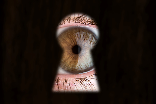 Women's brown eye looking through the keyhole. The concept of voyeurism, curiosity, Stalker, surveillance and security