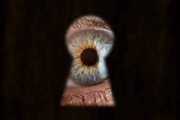 Male blue eye looking through the keyhole. Concept of voyeurism, curiosity, Stalker, surveillance and security stock photo