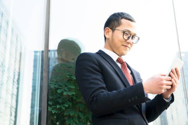 istock businessman holding smartphone against glass wall 899060480