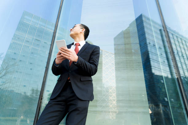 istock businessman holding smartphone against glass wall 899061448