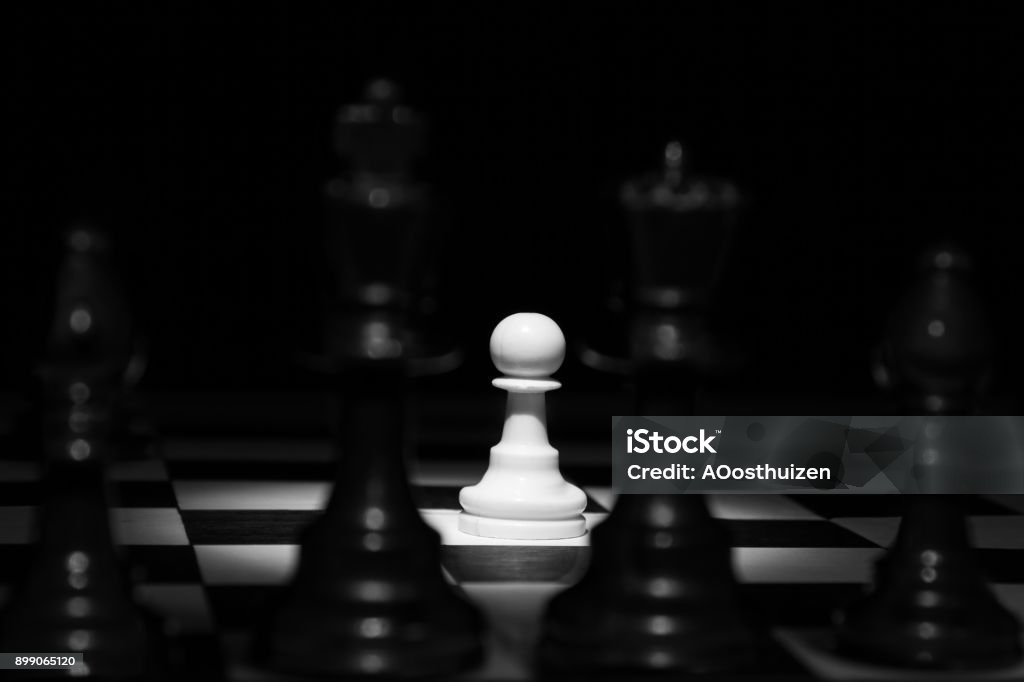 White pawn standing alone in spotlight on chess board between black pieces artistic conversion Abstract Stock Photo