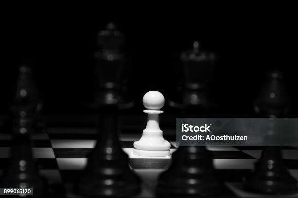 White Pawn Standing Alone In Spotlight On Chess Board Between Black Pieces Artistic Conversion Stock Photo - Download Image Now