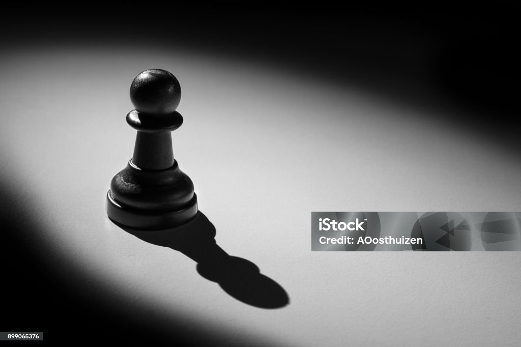 Chess pawn standing in a spotlight that make a shadow with darkness Pawn - Chess Piece Stock Photo