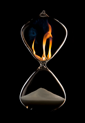 Hourglass in a dark studio with rim lighting and fire flames in the top