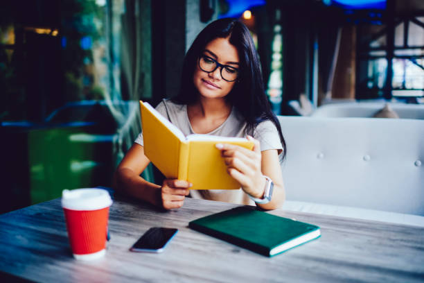 istock Pensive young student in eyeglasses reading favorite book during coffee break spending time on autodidact, concentrated businesswoman checking working schedule in dairy during free time in cafe 899074568