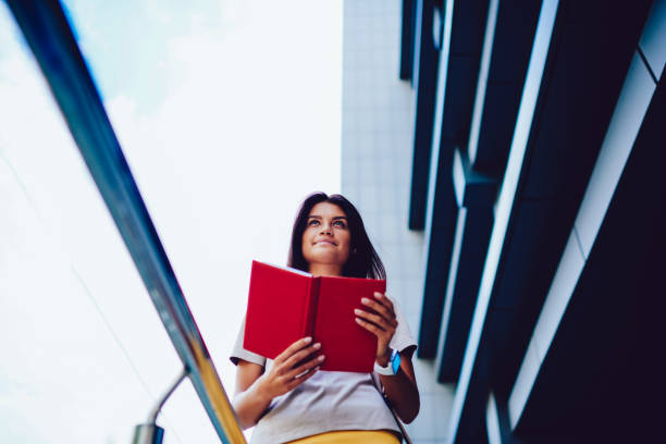 istock Young brunette student preparing for exams analyzing information strolling to college on street, attractive hipster girl holding notebook with checklist of goals motivated for reaching success 899074574