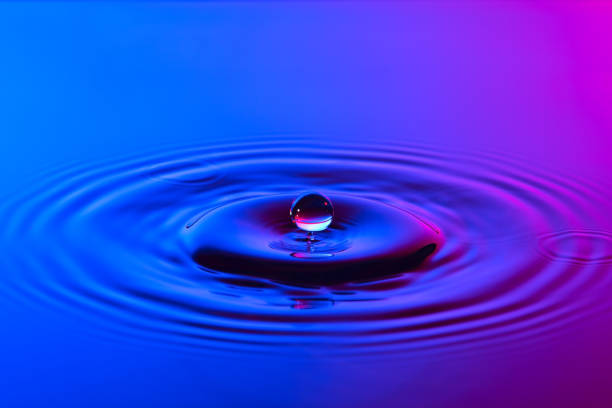 istock Water drop close up with concentric ripples on colourful blue and pink surface 899075156