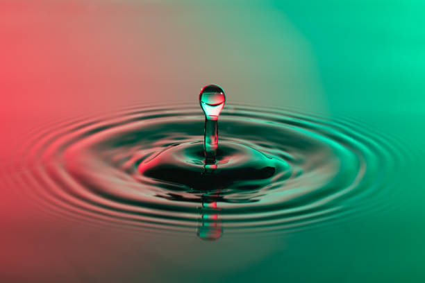istock Water drop close up with concentric ripples on colourful red and green surface 899075432
