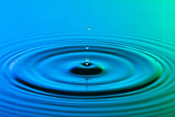 istock Water drop close up with concentric ripples on colourful blue and green surface 899075436