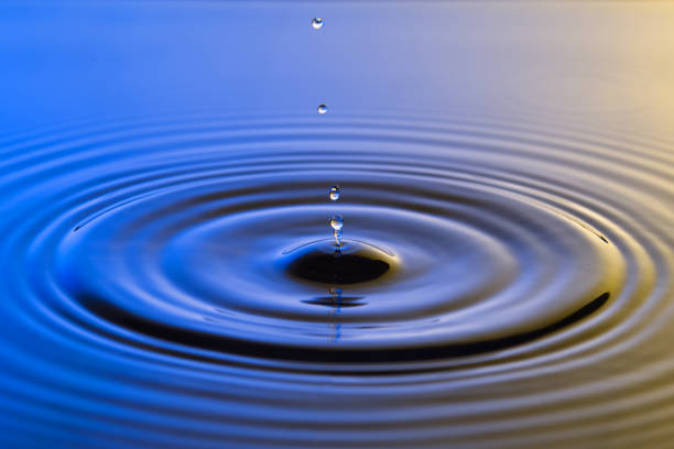 istock Water drop close up with concentric ripples on colourful blue and yellow surface 899077620