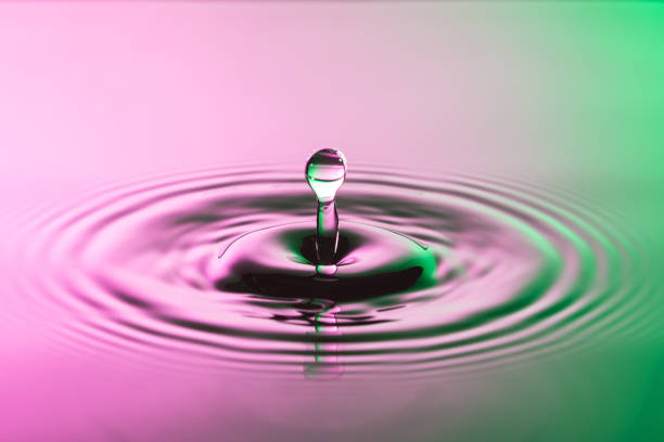 Water drop close up with concentric ripples on colourful pink and green surface