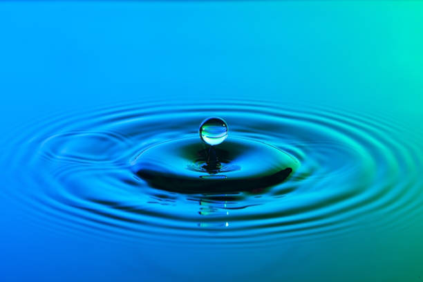 istock Water drop close up with concentric ripples on colourful blue and green surface 899077672