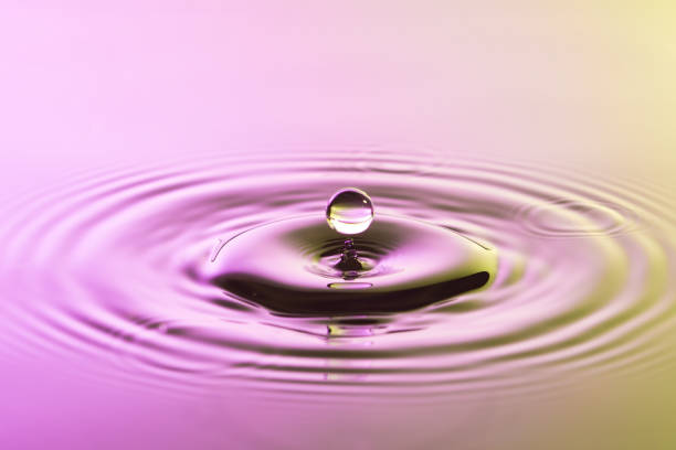 istock Water drop close up with concentric ripples on colourful pink and yellow surface 899077682