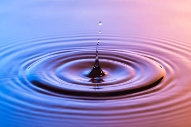 istock Water drop close up with concentric ripples on colourful blue and amber surface 899077810