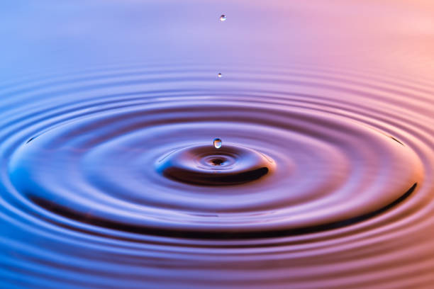 Water drop close up with concentric ripples on colourful blue and amber surface