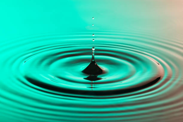 istock Water drop close up with concentric ripples on colourful pink and green surface 899077940