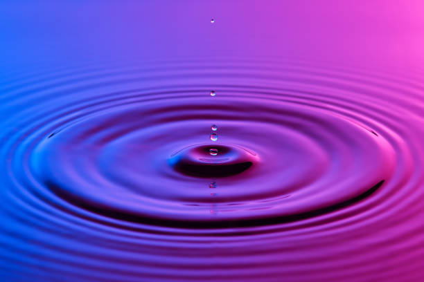 istock Water drop close up with concentric ripples on colourful blue and pink surface 899078364