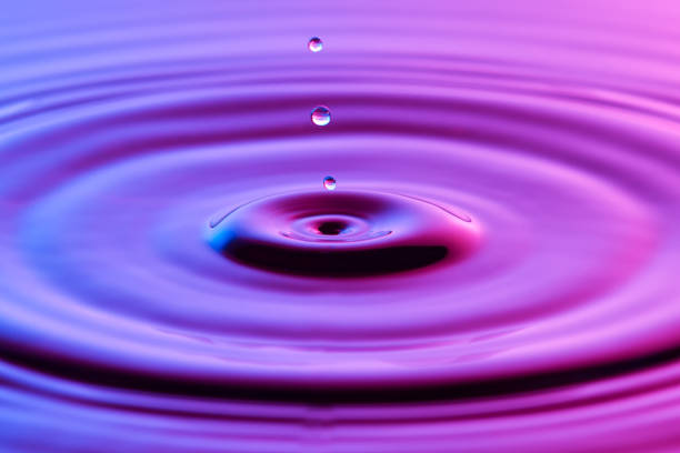 istock Water drop close up with concentric ripples on colourful blue and pink surface 899078374