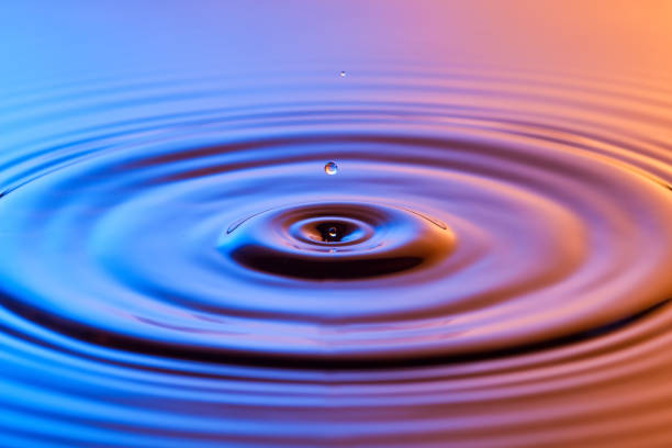 istock Water drop close up with concentric ripples on colourful blue and amber surface 899078508