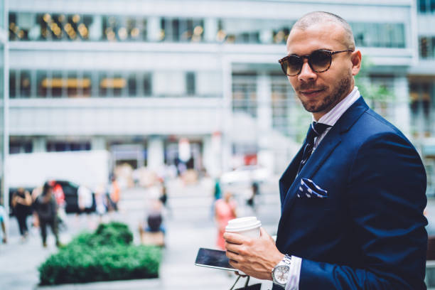 ritratto di uomo d'affari in elegante abito che trascorre il tempo libero all'aperto con caffè per andare in piedi sull'area pubblicitaria, boss serio con occhiali da sole eleganti in attesa di personal shopper guardando la macchina fotografica - personal shopper foto e immagini stock