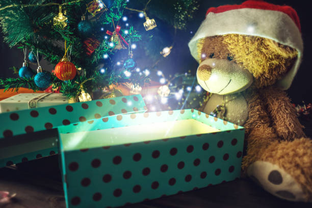istock A Teddy bear opens a gift on background glowing Christmas tree. Concept of new year's eve Magic 899081910