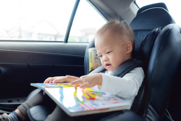 Cute little Asian 18 months / 1 year old toddler baby boy child sitting in car seat holding and enjoy reading book stock photo