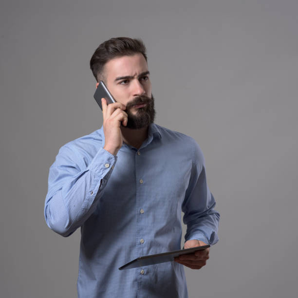 istock Young confident bearded business man talking on the cellphone holding tablet computer and looking away 899096212