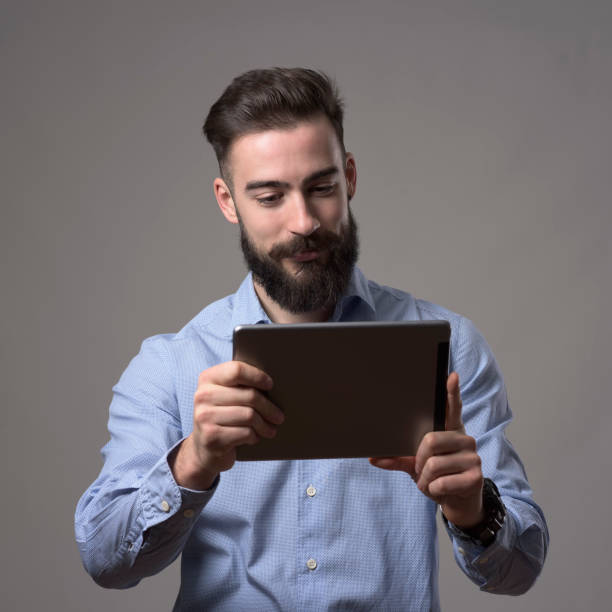 istock Young happy bearded man holding and reading e-book from touch pad tablet computer 899096718