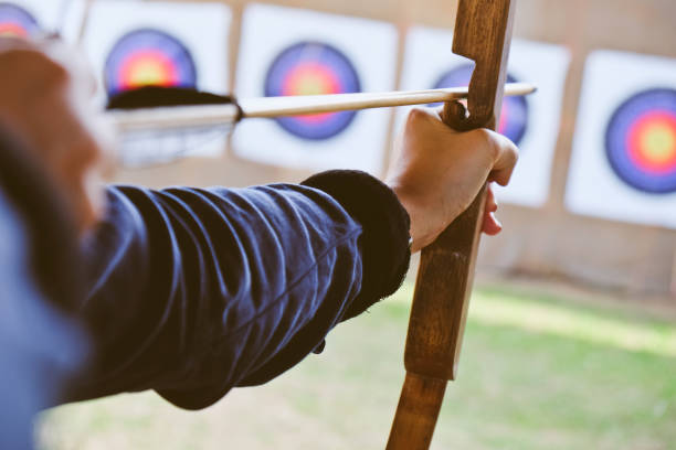 archer tiene su bow apuntando a un objetivo - tiro con arco fotografías e imágenes de stock