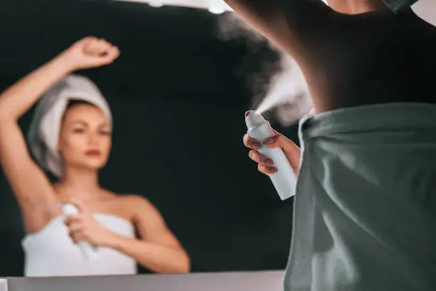 Attractive young woman in bathroom after shower is standing in front of mirror with deodorant in hands. Women care.