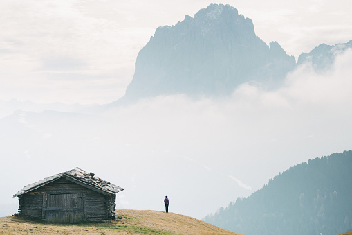 Silhouette of young Caucasian man standing near the hut with view of Dolomites mountains, Italy