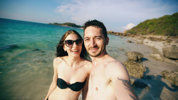 istock Young happy couple talking with friends through internet using smartphone in ocean beach 899113624