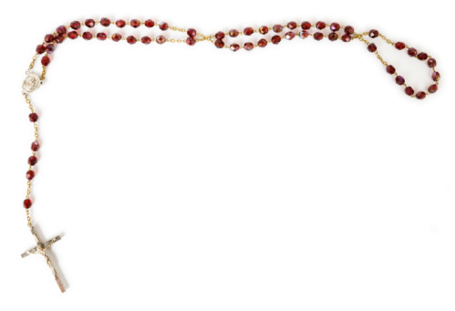 Rosary with white beads laying on a white wood table with a branch with white flower blossoms and green leaves with copy space