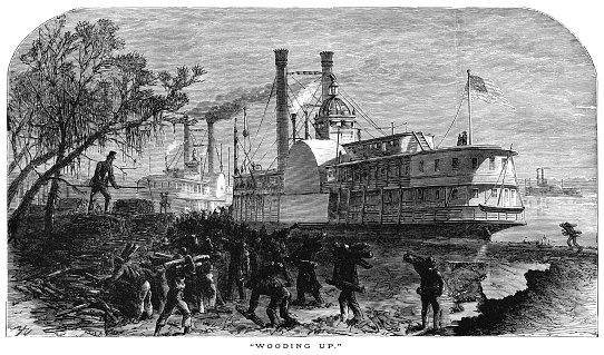 Workmen moving piles of logs from a quayside onto a Mississippi paddle steamer to fuel its upcoming journey along the river in the Deep South of the United States, as indicated by the Spanish Moss hanging from a tree.