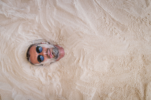 Man lying on the beach with his all body covered with sand
