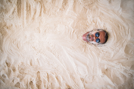 Man lying on the beach with his all body covered with sand