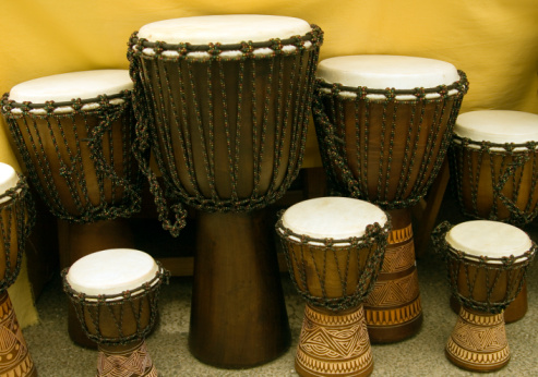 Pair of wooden bongo drums with handing carvings.  Turquoise background.  Sitting on marble top table.  African drums.