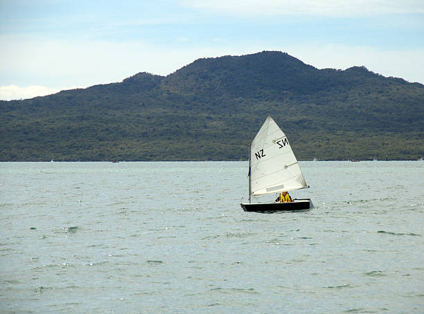 New Zealand Optimist Lone optimist dinghy in front of Rangitoto Island on a tranquil Sunday morning rangitoto island stock pictures, royalty-free photos & images