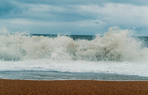 A storm whips up large waves hitting a pebbled beach.
