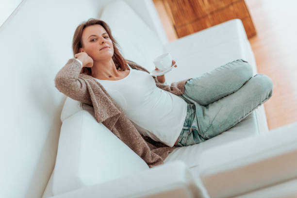 istock beautiful young middle aged woman resting, drinking tea and reading on a white sofa surrounded by the white interior 899225834