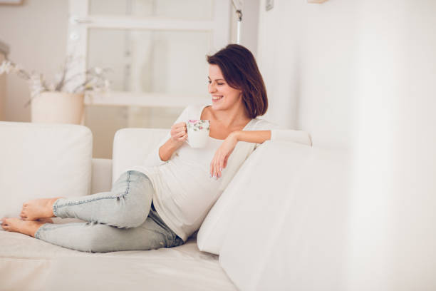 istock beautiful young middle aged woman resting, drinking tea and reading on a white sofa surrounded by the white interior 899230948