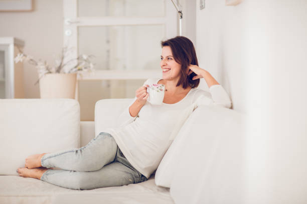 istock beautiful young middle aged woman resting, drinking tea and reading on a white sofa surrounded by the white interior 899231146