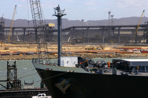 Bulk carrier moored at coal loading port of Gladstone, Queensland, stockpiles and conveyor belts in background.