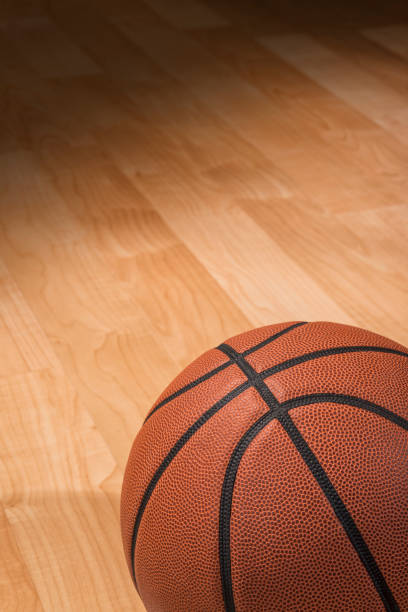 Basketball sitting in the spotlight on a court A close-up of a basketball sitting on a wooden basketball court illuminated by a spotlight college basketball court stock pictures, royalty-free photos & images