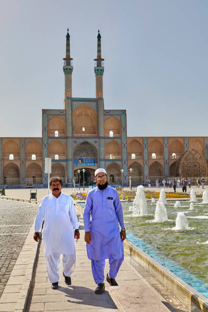 Islamic clergymen stroll near mosque on sunny day, Yazd, Iran. Yazd, Iran - April 22, 2017: Two Islamic clerics stroll through the square with a fountain in a sunny day on the background of Amir Chakhmaq mosque. mullah photos stock pictures, royalty-free photos & images