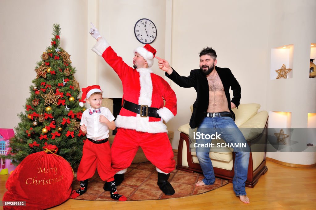 Árbol De Navidad Bolso Del Regalo Chimenea Hombres Vestidos Como Santa Muchacho De Pantalones Rojos Y Medias Alta Y Un Hipster En La Chaqueta De Terciopelo En El Torso Desnudo Baile Juega Árbol De Navidad Bolso Del Regalo Chimenea Hombres Vestidos Como Santa Muchacho De Pantalones Rojos Y Medias Alta Y Un Hipster En La Chaqueta De Terciopelo En El Torso Desnudo Baile Juega