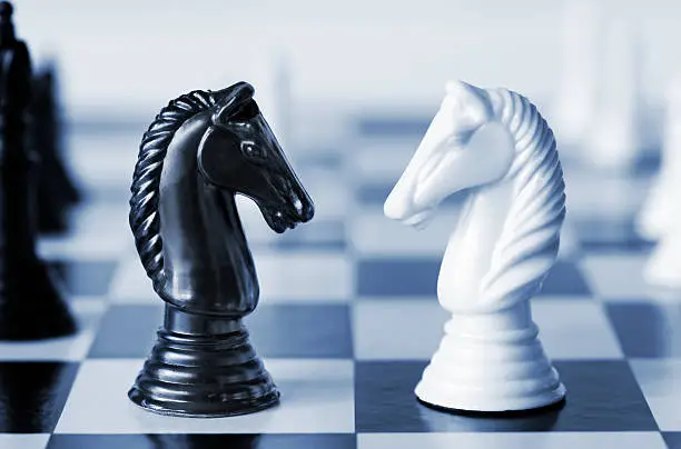 Photo of Black versus white chess knights on a board