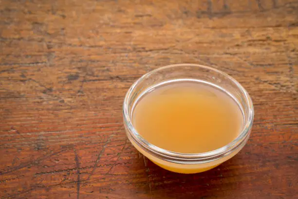 unfiltered, raw apple cider vinegar with mother  - a small glass bowl against rustic wood with a copy space