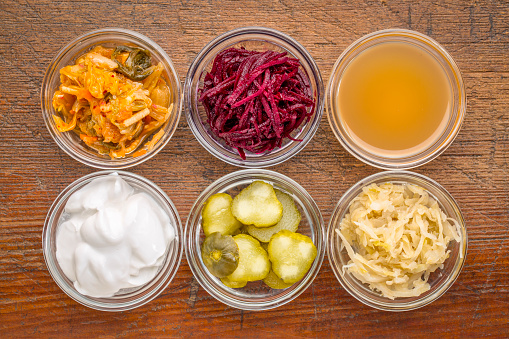 a set of fermented food great for gut health - top view of glass bowls against rustic wood:  kimchi, red beets, apple cider vinegar, coconut milk yogurt, cucumber pickles, sauerkraut